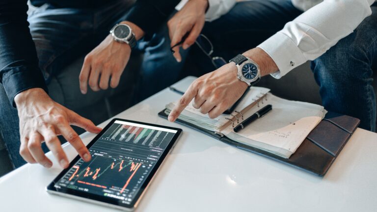 INDUSTRIES Close-up of professionals discussing stock charts on a tablet with notes and pens on a table.